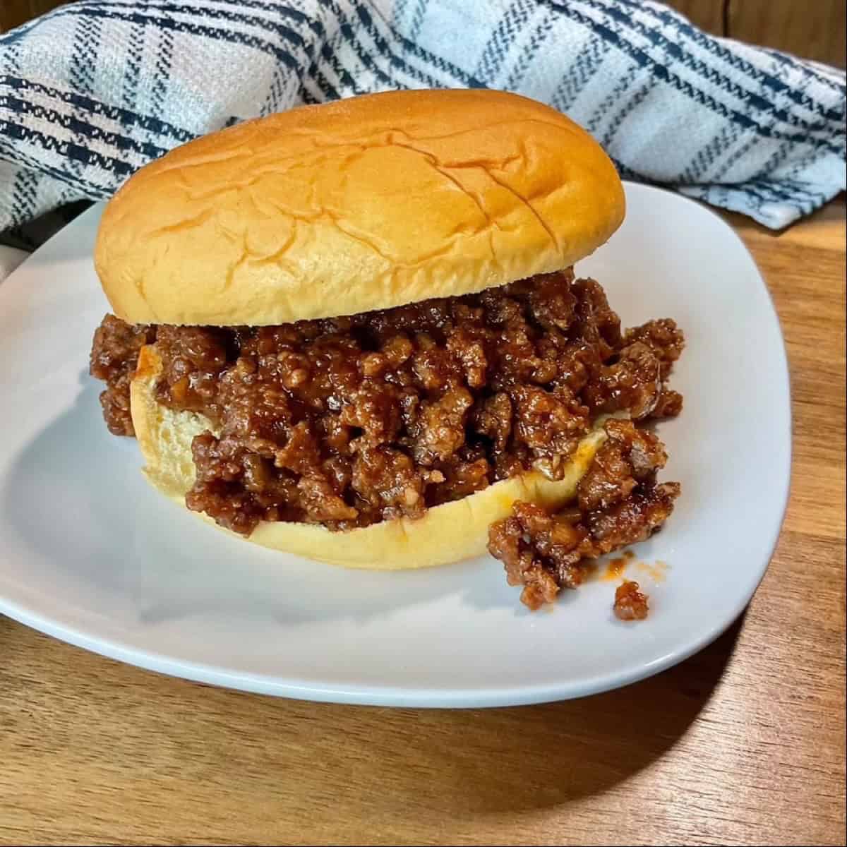 sloppy joe sandwich on white plate with blue and white napkin.